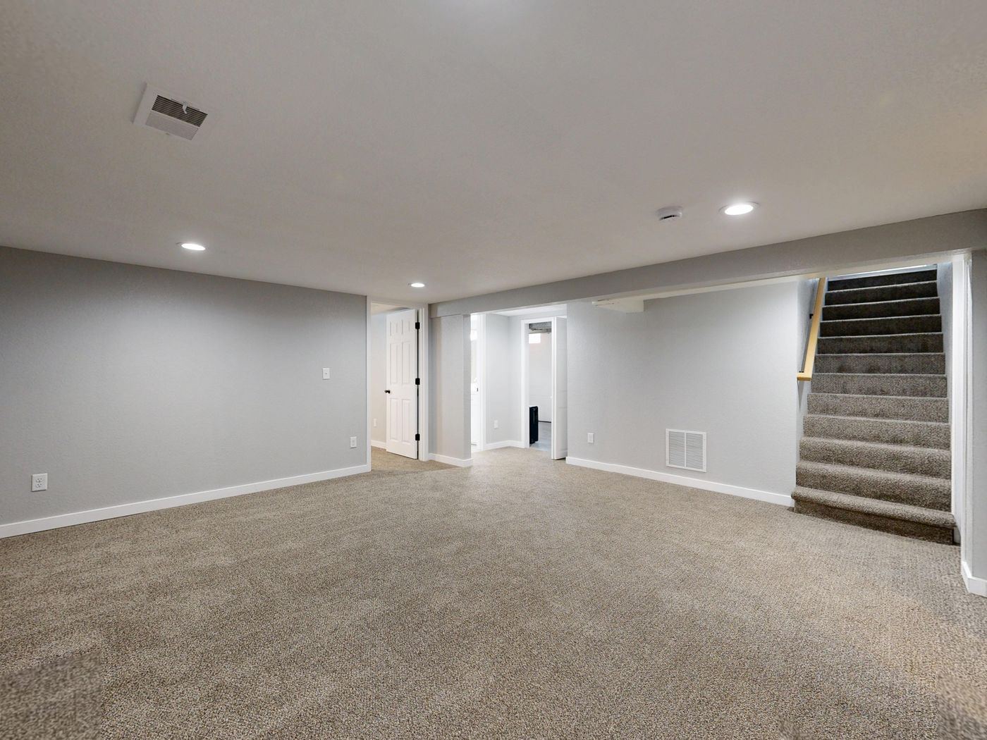 Finished basement with carpet, painted walls, a carpeted stair, and white doors.