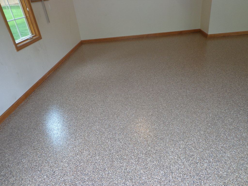 Speckled epoxy flake floor coating in a garage room with a window and wood baseboard.