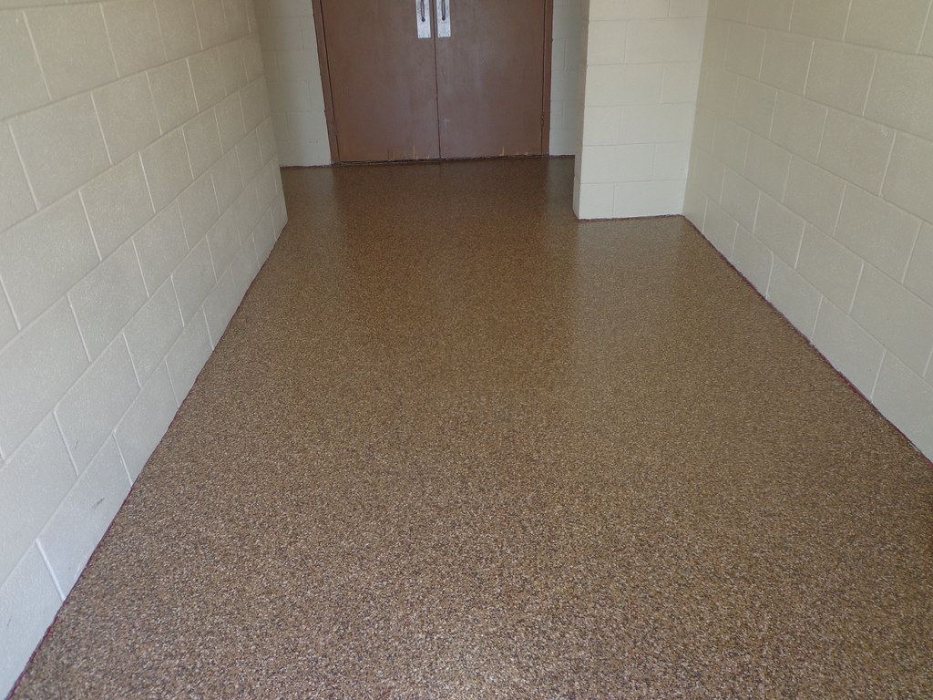 Tan epoxy flake floor in a narrow hallway with block walls and a brown door.