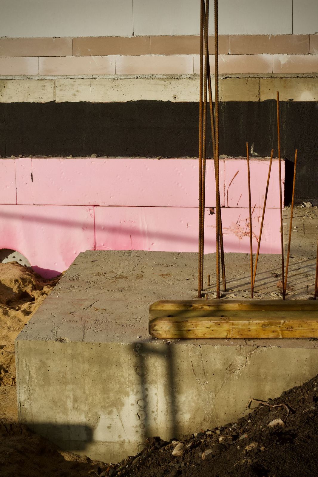 Concrete foundation footing with vertical rebar and rigid foam insulation on the wall behind it.