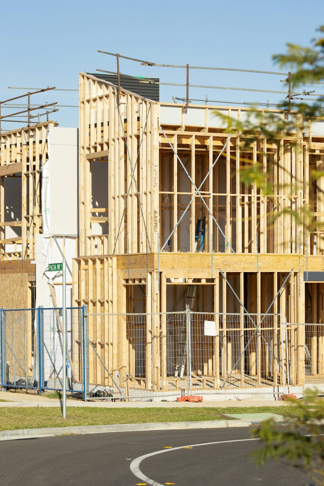 Wood-framed house under construction with open stud walls, sheathing, and roof framing.