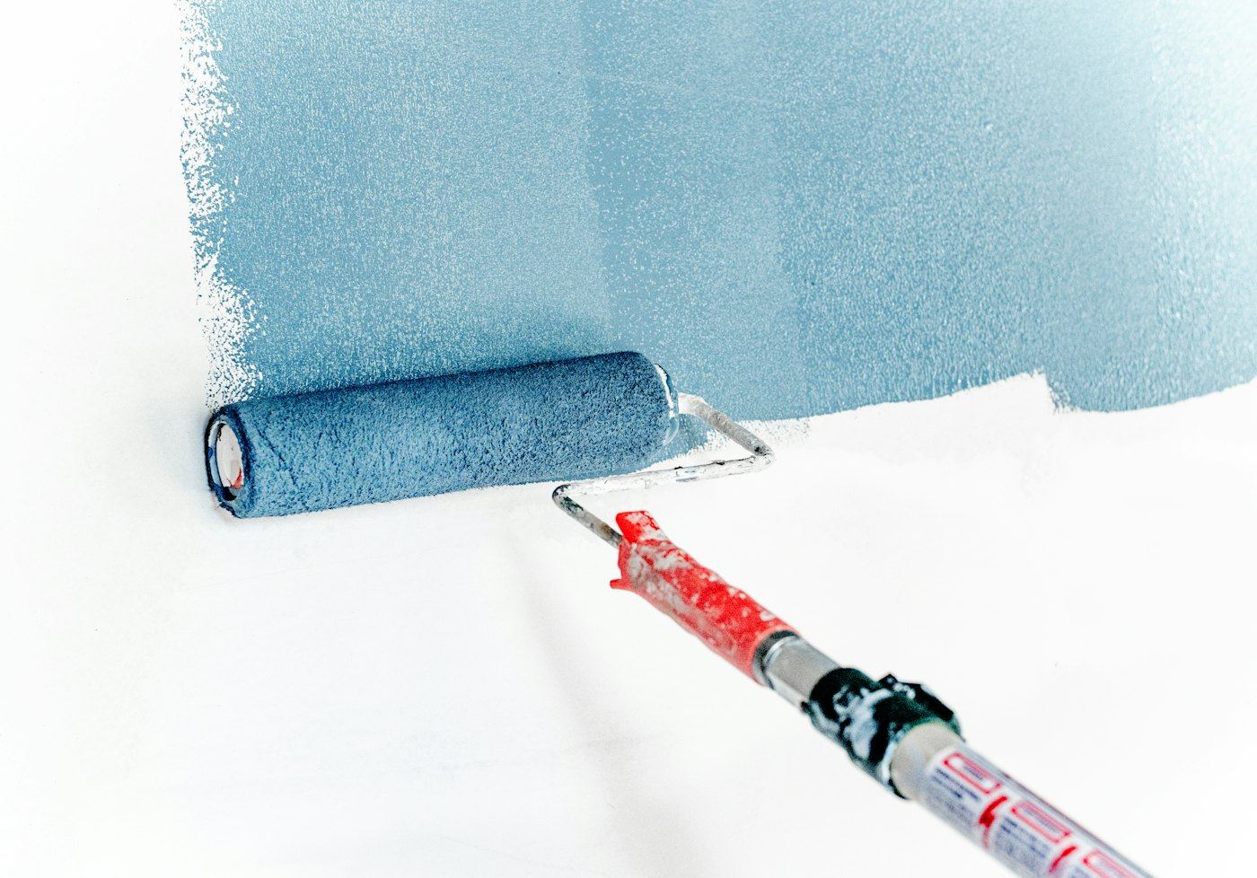 Paint roller spreading blue paint across a white wall.