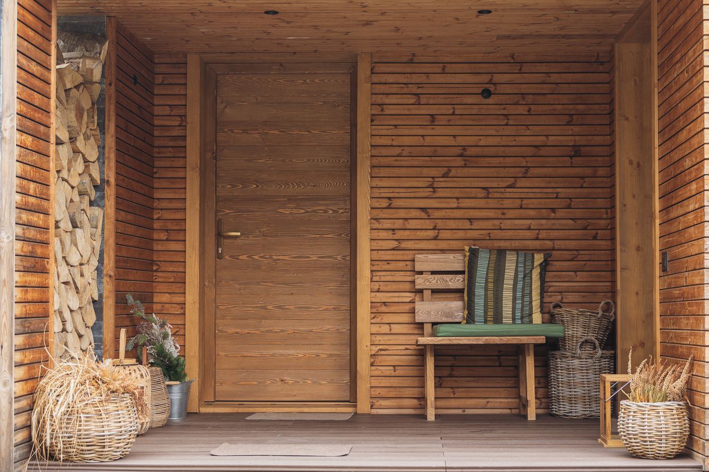 Covered wooden porch with a wood door, bench, and decking at the entry.