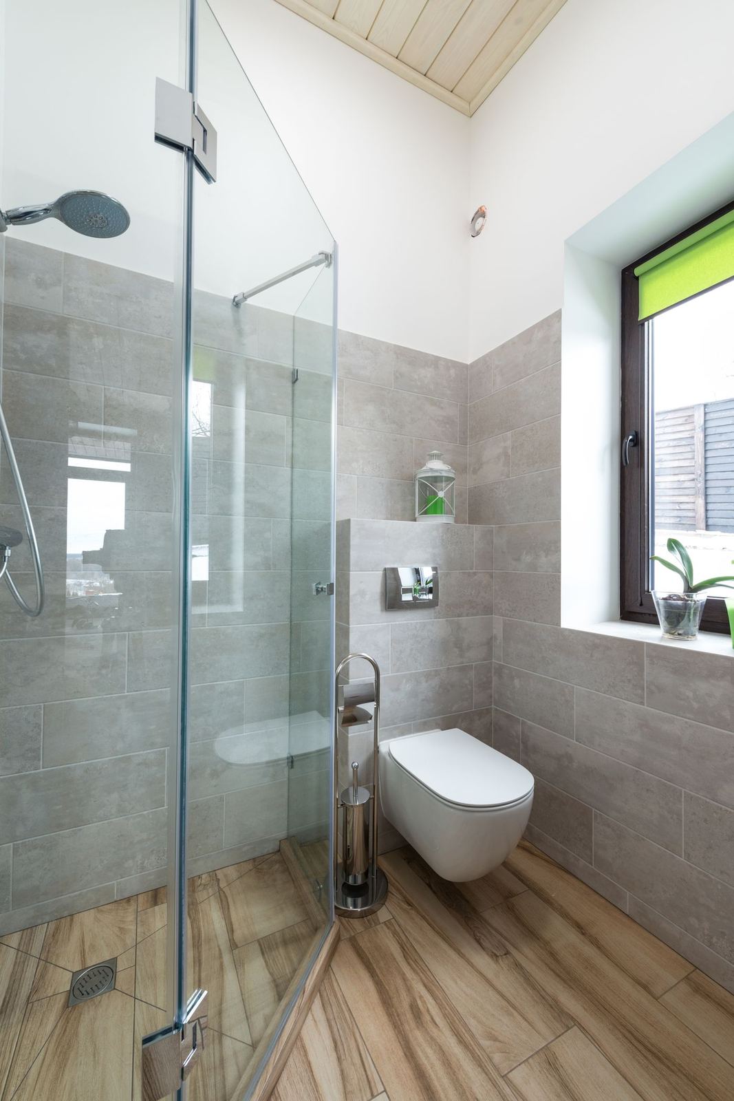 Shower with large gray wall tile, a glass panel, and wood-look floor tile.
